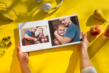 woman hands holding a family photo album agains on a yellow background. summertime. flat lay