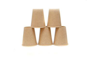 Brown paper cup for coffee, tea, a drink from environmental materials on a white background. The male hand builds a pyramid of cups in macro and overall plan. Place for text on the left and right.