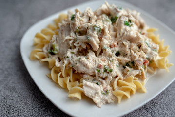 Crack chicken slow cooked dish over egg  pasta on a white plate 