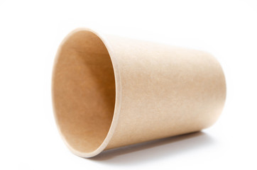 Brown paper cup for coffee, tea, a drink from environmental materials on a white background. One paper cup lies on its side and a shadow falls from it. glass with a neck sideways on a gray background