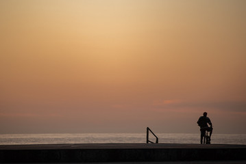 A man on his bicycle watches the sunrise on the beach.