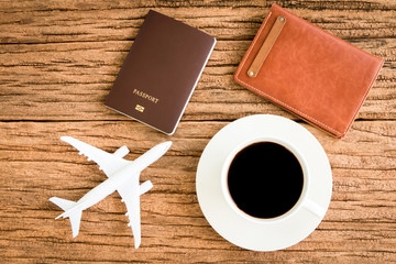 Passport and black coffee and a wallet and a plane model put on the wood texture for travel planning concept.