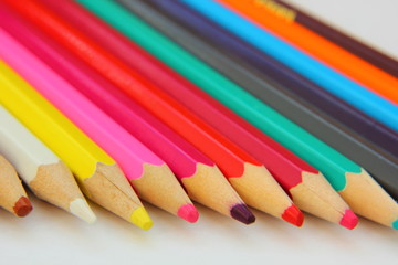 Color pencils lie in a row on white paper.