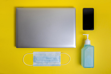 mask, disinfectant, computer and phone on yellow