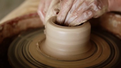 Close up footage of a woman sitting at pottery wheel in ceramics studio shaping clay vase - shot in slow motion. Front view. Unrecognizable person