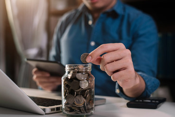 Male businessman hand puting coins in glass for saving money. concept finance and accounting in the home.