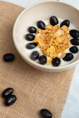 Close up a bowl of fresh grapes and yogurt with cornflakes served on a light blue background