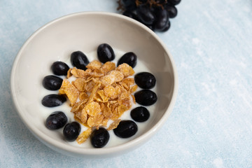 Close up a bowl of fresh grapes and yogurt with cornflakes served on a light blue background