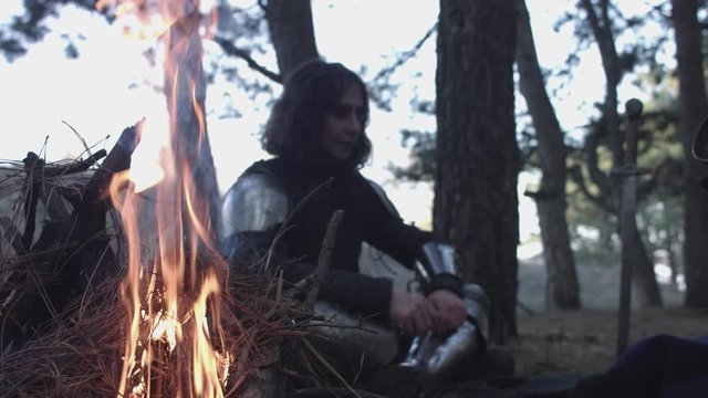 Two medieval knights in armor sitting near bonfire and devide production