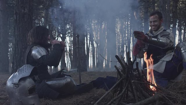 Two medieval knights sitting near bonfire and devide production
