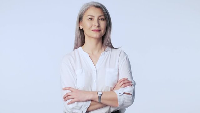 A dreaming old mature woman with long gray hair wearing formal business clothes is smiling and looking aside isolated over white background in studio