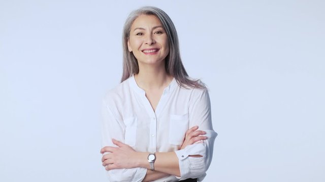 A happy positive old mature woman with long gray hair wearing formal business clothes is laughing and looking aside isolated over white background in studio