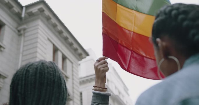 Women holding up a rainbow colored flag at gay parade.  Group of people in gay pride march
