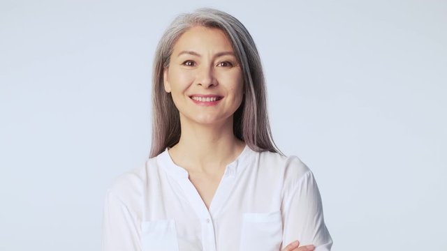 A friendly pleased old mature woman with long gray hair wearing formal business clothes is smiling standing isolated over white background in studio