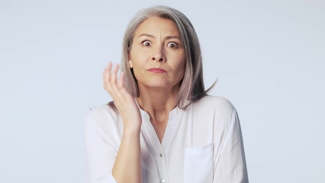 A serious confused old mature woman with long gray hair wearing formal business clothes is thinking about something isolated over white background in studio