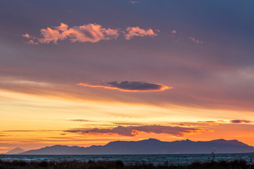 Sun has set down to the West with curly clouds near the fishermen village of Porto Lagos, Northern Greece. Mountain range and sea water in darkness. Blurred bushes in foreground