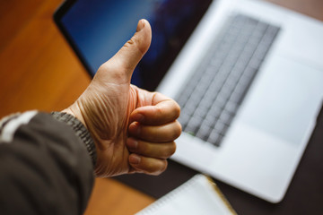 Young man keeps thumb up on a laptop background.