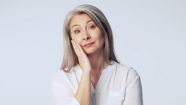 A frustrated old mature woman with long gray hair wearing formal business clothes is looking shocked and disappointed isolated over white background in studio