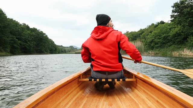 Rear view of man paddling canoe on cloudy day, slow motion