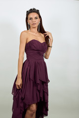 Young Attractive Woman Brunette In Purple Stylish Dress, With A Crown On Head On White Background, Confident Female Posing For The Camera. Concept Of People Models. Wide Angle