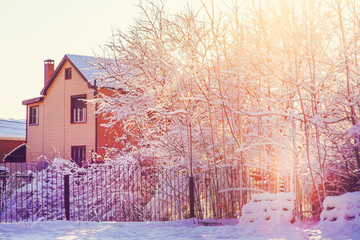 A house, a fence, a lot of snow on the trees and on the ground against the background of the sunset.