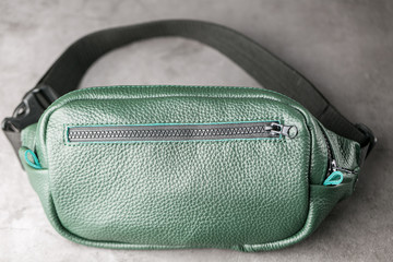 Belt bag made of dark green textured leather, banana on a gray background.