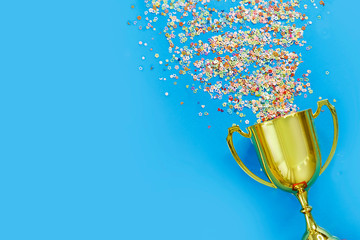 image of little gold cup , concept for winning or success. Golden trophy cup and streamers on blue background, top view with space for text - obrazy, fototapety, plakaty