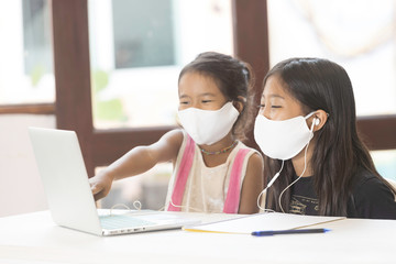 A pair of Asian schoolgirl girls wear a mask and are studying online at home during the corona virus epidemic.