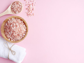 Fototapeta na wymiar Spa flatlay composition. Sea salt in wooden jar and scattered from spoon, bath towel on pink background. Copyspace, top view. Home care concept, relax and rest, bath procedure