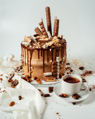 Chocolate cake decorated with various cookies and nuts on a glass plate standing on a white cloth. Food photography. Advertising and commercial close up design.