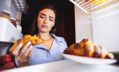 Thoughtful girl looking at croissant with doubt