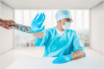 The doctor sits at his desk and refuses a bundle of hundred-dollar bills. Honest medicine concept.