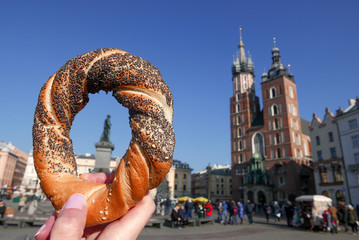 Woman hand holding bagel / obwarzanek, traditional polish snack. The Mariacka Tower in the background.
