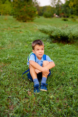A schoolboy sits on the green grass in the park and look up.