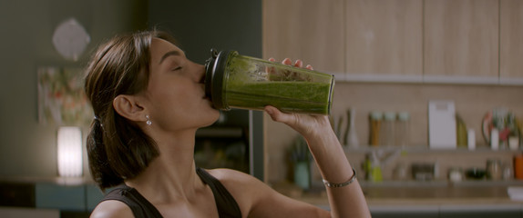 Portrait of fit female drinking green juice detox cocktail in the kitchen at home. Shot with 2x...
