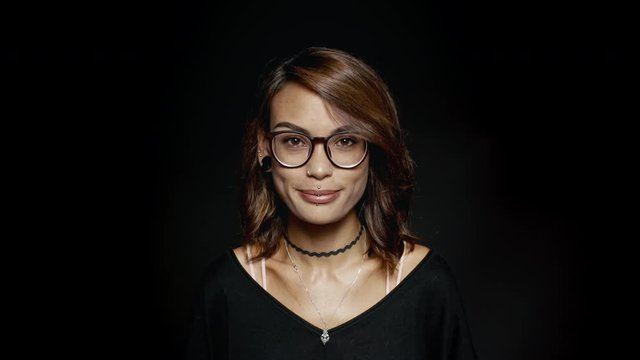 Smiling woman in eyeglasses on black background. Fashionable woman with pierced lips looking at camera and smiling.
