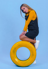 pretty young blonde model girl in sportswear posing next to car yellow tires in blue backround
