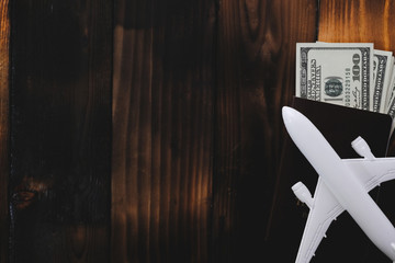 White model of passenger plane with passport and money on old wooden background. Travel saving and planning concept - Top view.