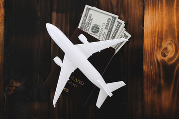 White model of passenger plane with passport and money on old wooden background. Travel saving and planning concept - Top view.