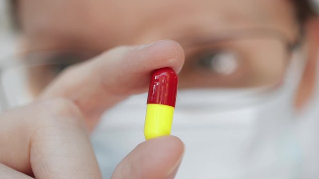Medicine pill. Extreme macro closeup of person wearing mask and glasses holding up a red and yellow capsule