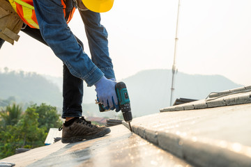 Construction engineer wear safety uniform install the new roof,Roofer using air or pneumatic nail gun and installing concrete roof tile on top roof. © visoot