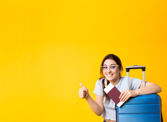 Excited caucasian traveler woman in t-shirt,sunglasses with blue suitcase making thumb up sign....