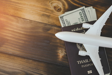 White model of passenger plane with passport and money on old wooden background. Travel saving and planning concept - Top view.