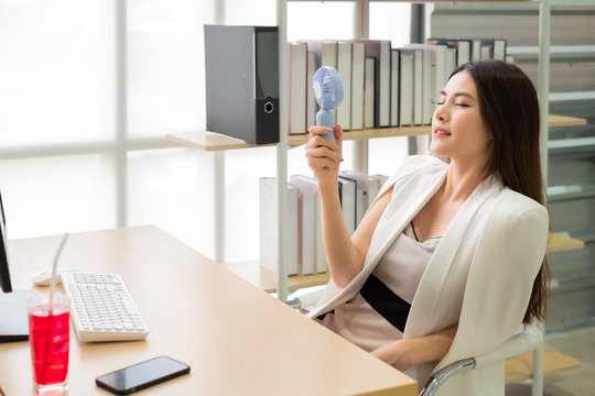 Asian Woman Woking At Her Desk Office With Fan And Water In Summer Time