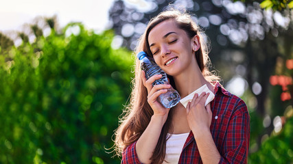 Happy satisfied woman wipes neck with a napkin and cooling with a bottle of cold refreshing water...