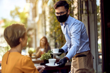 Waiter serving coffee to female guest while wearing protective face mask.