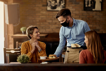 Waiter with protective face mask serving food to customers in a pub.