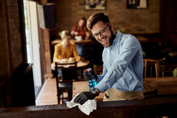 Young cheerful waiter having fun while cleaning cafe.