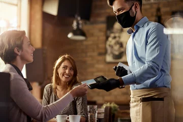 Selbstklebende Fototapete Kneipe Weibliche Kunden, die kontaktlos an einen Kellner in einem Café bezahlen.