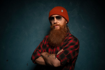 Red bearded man with orange hat and plaid shirt on dark cyan background